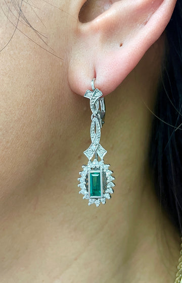 Platinum emerald and diamond drop earrings with rectangular green center stone and halo sparkle