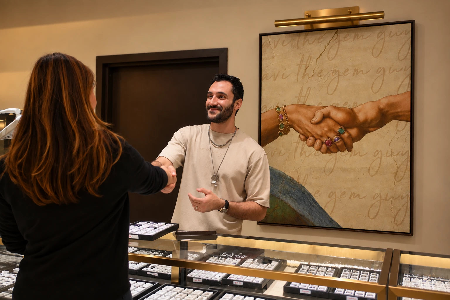 Avi shaking hands with a customer across the showroom counter, the Avi The Gem Guy painting behind him