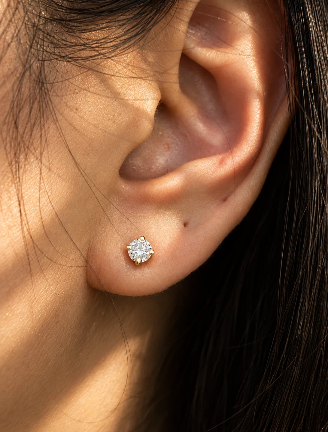 Round diamond stud in a gold four-prong setting, worn in an ear