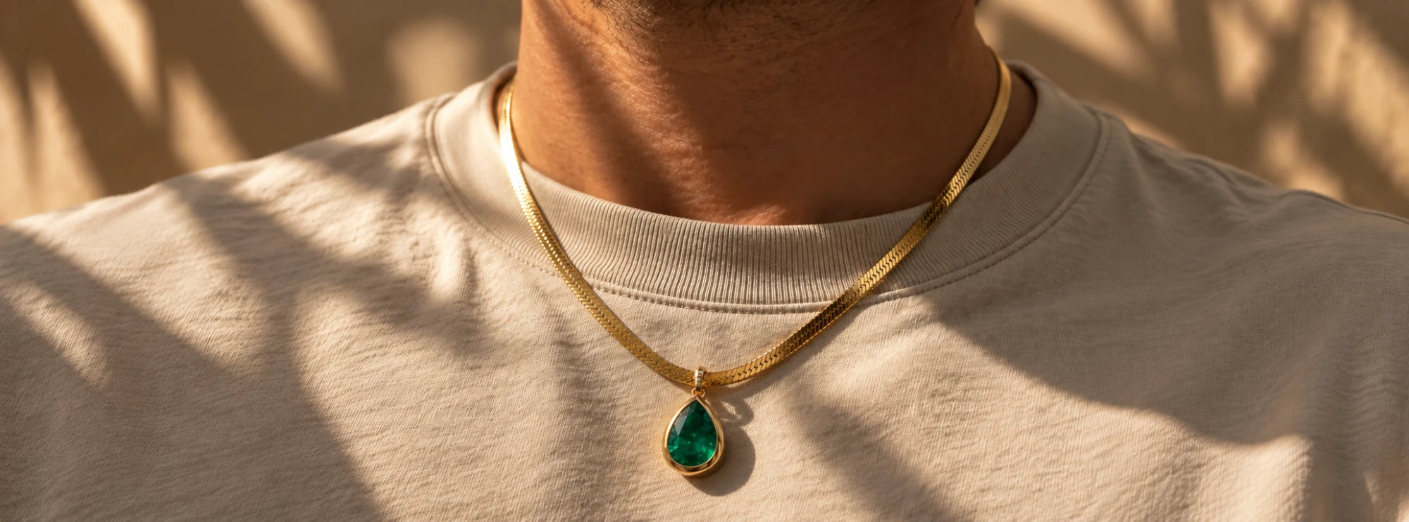 Emerald pear pendant on a gold herringbone chain, worn over a cream t-shirt
