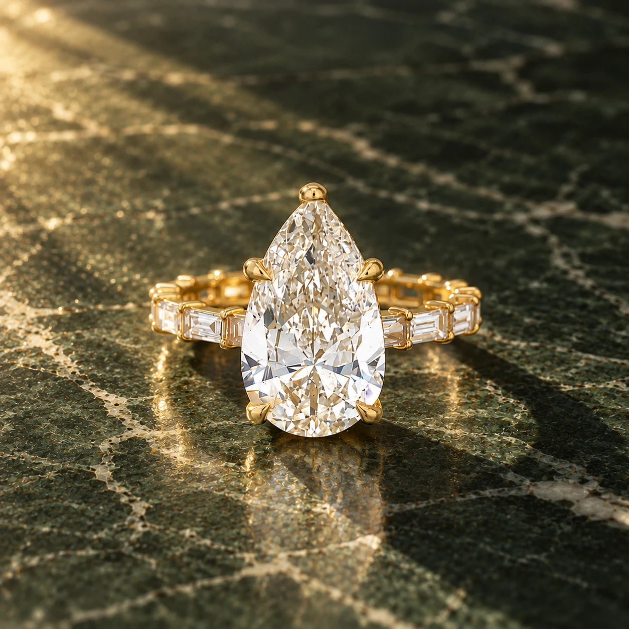 A pear-cut diamond engagement ring in yellow gold with a baguette eternity band, on dark green marble